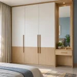 Compact bedroom with a full-height light oak and white three-door wardrobe, integrated narrow dressing mirror with drawer, daylight and pale blue wall. Entire wardrobe visible.